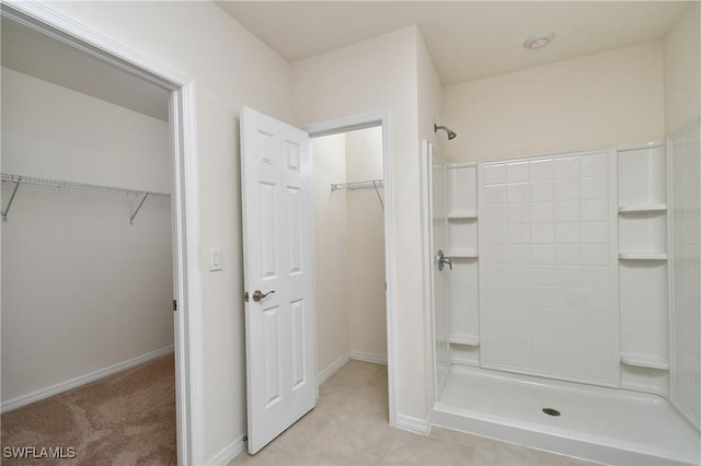 full bath featuring a tile shower, a walk in closet, and baseboards