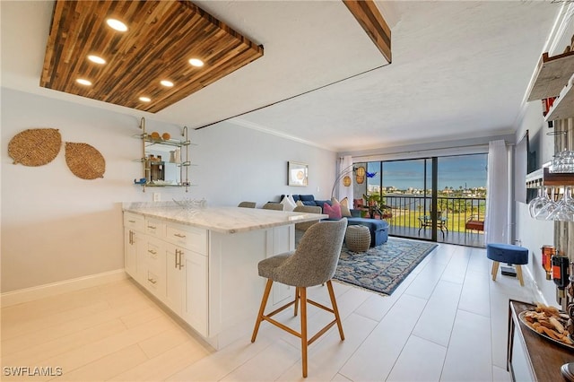 260 Southbay Dr Unit 102, Naples, FL 34108 - kitchen with a peninsula, white cabinets, light stone counters, baseboards, and a breakfast bar area