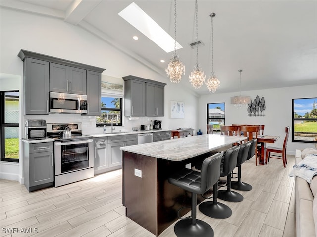 kitchen with appliances with stainless steel finishes, gray cabinets, a sink, a skylight, and a center island