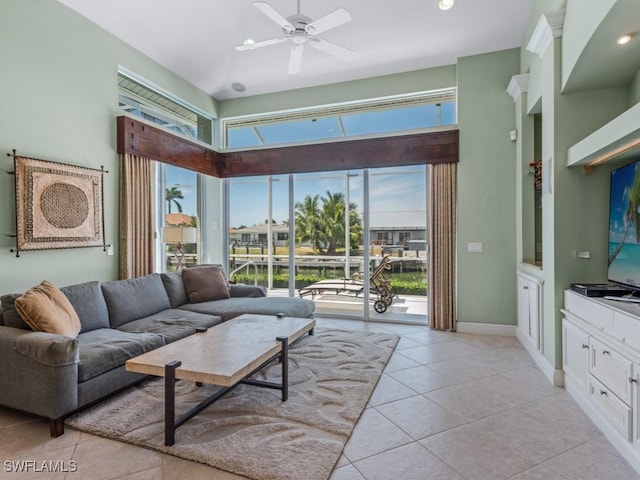 living area featuring ceiling fan, light tile patterned floors, a towering ceiling, and baseboards