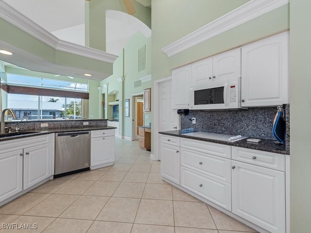 kitchen with white appliances, a sink, backsplash, light tile patterned floors, and white cabinets