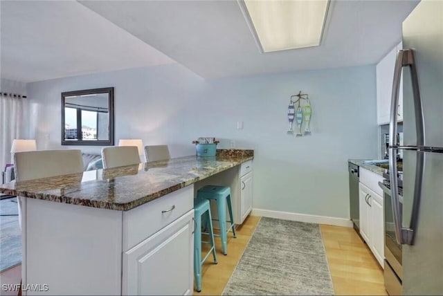 260 Southbay Dr Unit 103, Naples, FL 34108 - kitchen featuring a peninsula, white cabinetry, light wood-type flooring, stainless steel appliances, and dark stone counters