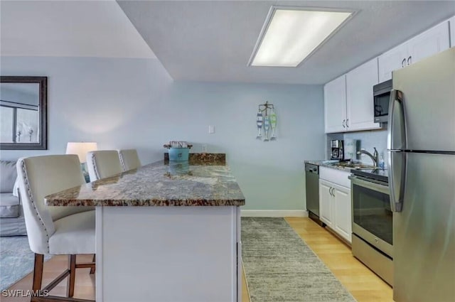 260 Southbay Dr Unit 103, Naples, FL 34108 - kitchen featuring appliances with stainless steel finishes, a peninsula, a breakfast bar area, white cabinets, and light wood-style flooring