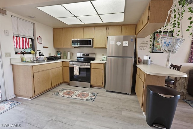 kitchen with appliances with stainless steel finishes, a peninsula, light countertops, a sink, and light wood-type flooring