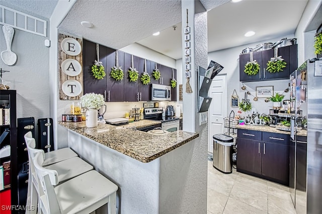 13160 Bella Casa Cir Unit 2115, Fort Myers, FL 33966 - kitchen with stainless steel appliances, light stone countertops, a textured wall, a kitchen bar, and a textured ceiling