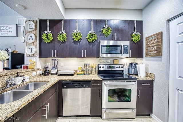 13160 Bella Casa Cir Unit 2115, Fort Myers, FL 33966 - kitchen featuring appliances with stainless steel finishes, a textured wall, a sink, light stone counters, and dark brown cabinets