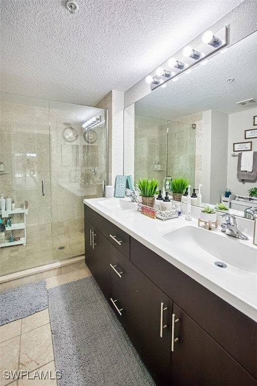 13160 Bella Casa Cir Unit 2115, Fort Myers, FL 33966 - full bathroom with a stall shower, a textured ceiling, double vanity, and tile patterned floors