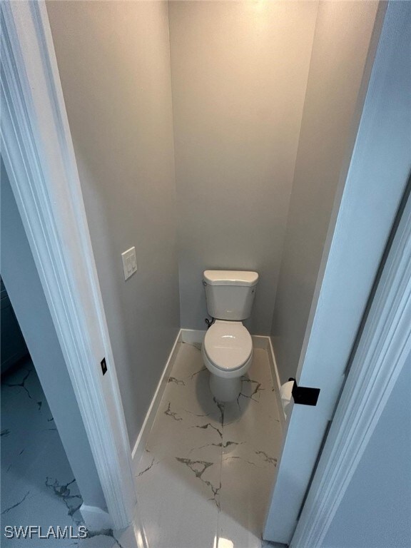 bathroom featuring marble look tiles, baseboards, and toilet