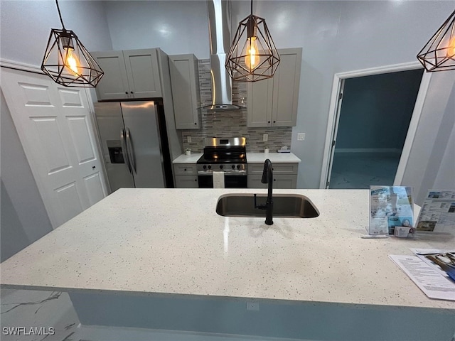 kitchen featuring stainless steel appliances, a sink, gray cabinets, light stone counters, and wall chimney range hood