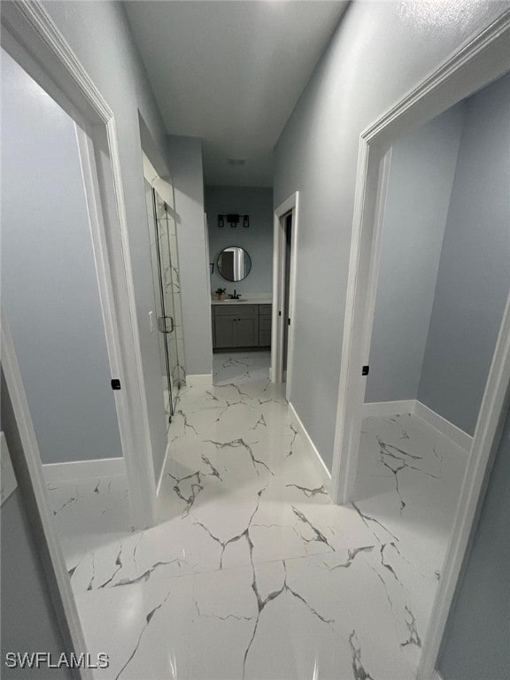 hall featuring light marble finish flooring, baseboards, and a sink