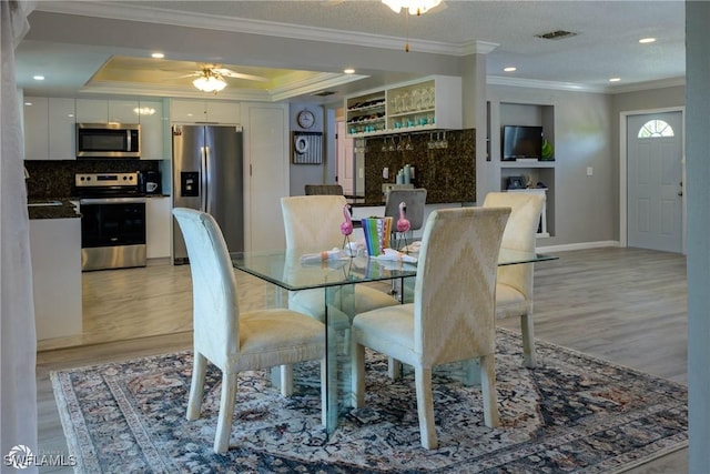 1303 Thompson St, North Fort Myers, FL 33903 - dining space with crown molding, light wood-style floors, a tray ceiling, ceiling fan, and baseboards