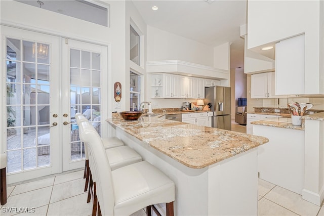 28839 Winthrop Cir, Bonita Springs, FL 34134 - kitchen featuring appliances with stainless steel finishes, a peninsula, light tile patterned flooring, light stone counters, and a towering ceiling