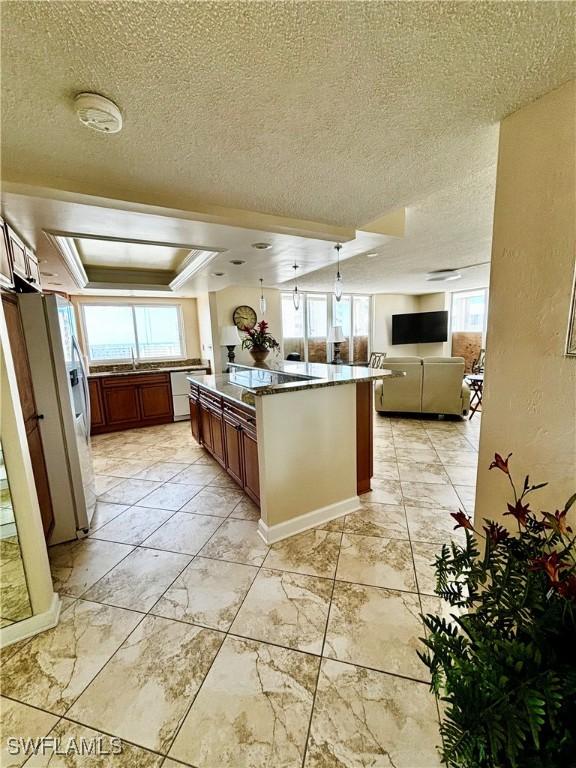 kitchen featuring open floor plan, a textured ceiling, white refrigerator with ice dispenser, a center island, and a raised ceiling