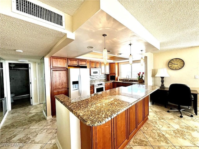 kitchen featuring white appliances, a textured ceiling, stone counters, brown cabinetry, and a sink