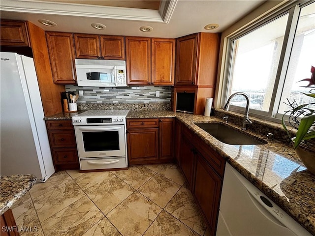 kitchen with white appliances, a sink, decorative backsplash, brown cabinets, and stone counters