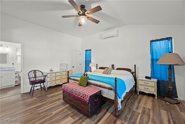 bedroom featuring a wall mounted AC, vaulted ceiling, wood finished floors, ensuite bath, and a ceiling fan