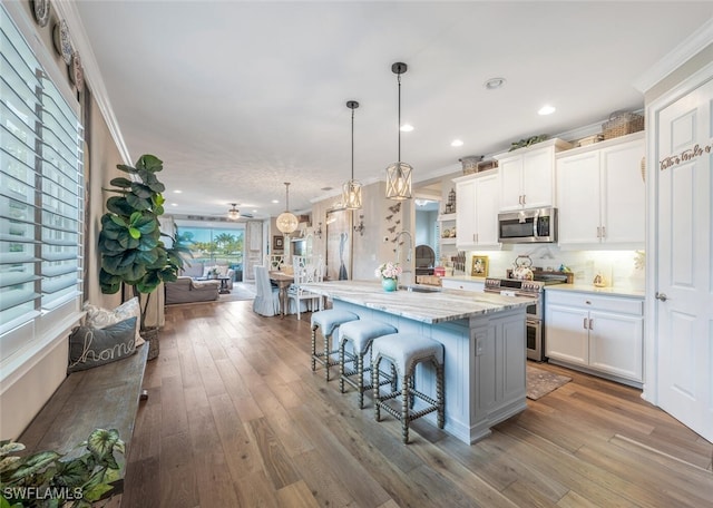 28268 Seasons Tide Ave, Bonita Springs, FL 34135 - kitchen featuring appliances with stainless steel finishes, ornamental molding, a kitchen bar, white cabinetry, and wood-type flooring