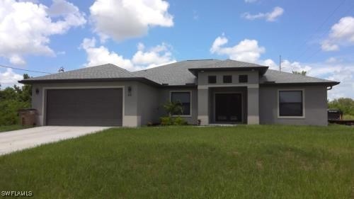 50 Sara Ave S, Lehigh Acres, FL 33976 - prairie-style home featuring driveway, an attached garage, stucco siding, and a front lawn