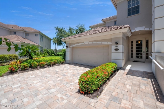 view of side of home featuring a tiled roof, stucco siding, decorative driveway, and a garage