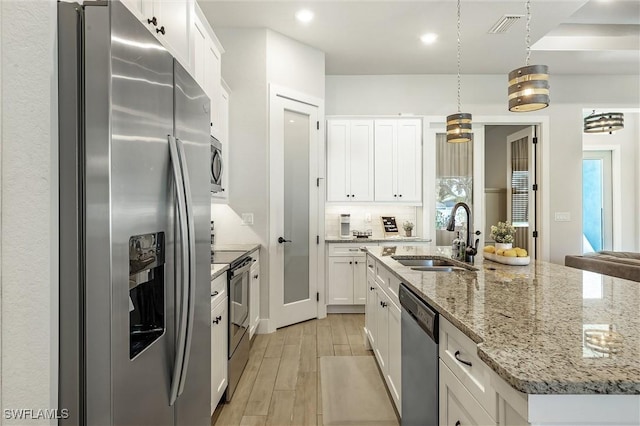 kitchen featuring stainless steel appliances, a sink, light wood-style flooring, white cabinets, and a kitchen island with sink