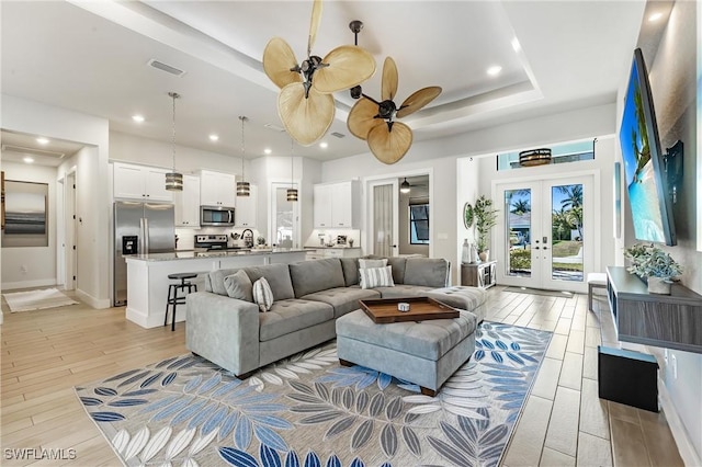 living area featuring french doors, ceiling fan, light wood finished floors, a raised ceiling, and recessed lighting