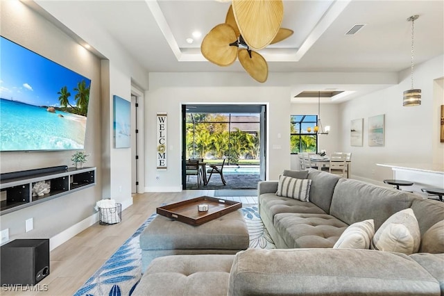 living room with a raised ceiling, light wood finished floors, ceiling fan, and baseboards