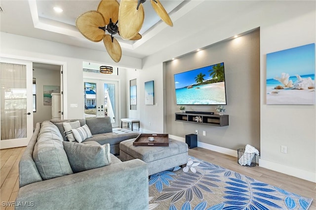 living area featuring wood finished floors, french doors, a tray ceiling, baseboards, and a ceiling fan