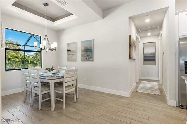 dining room featuring baseboards, light wood-type flooring, a chandelier, and a tray ceiling