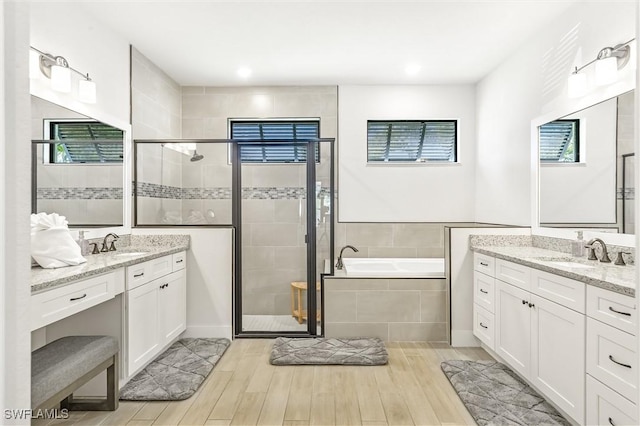 bathroom with a shower stall, a garden tub, two vanities, wood finished floors, and recessed lighting