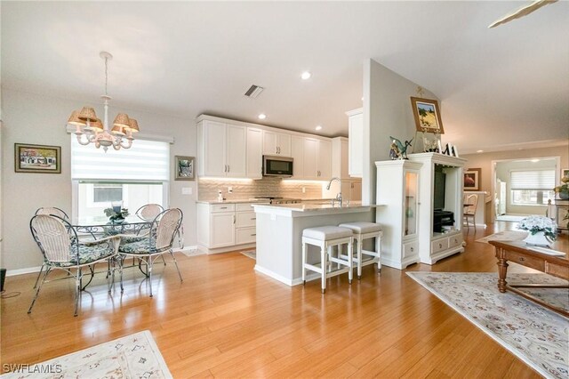 kitchen with stainless steel microwave, a kitchen breakfast bar, a chandelier, decorative backsplash, and white cabinetry