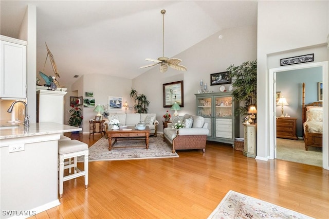 living area with a ceiling fan, light wood-style floors, high vaulted ceiling, and baseboards
