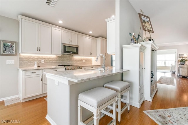 kitchen with stainless steel microwave, a sink, light wood-style floors, and recessed lighting