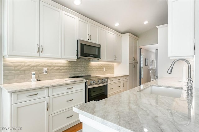 kitchen with appliances with stainless steel finishes, a sink, white cabinets, light stone countertops, and recessed lighting