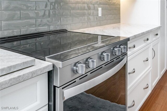 kitchen view of electric range, decorative backsplash, white cabinets, and light stone counters