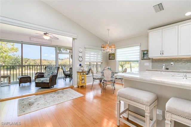 kitchen featuring lofted ceiling, a chandelier, white cabinetry, light stone counters, and plenty of natural light