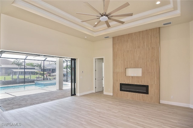 unfurnished living room featuring a tray ceiling, ornamental molding, ceiling fan, light wood-type flooring, and a sunroom