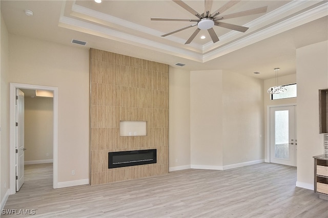 unfurnished living room with a raised ceiling, ornamental molding, light wood-style flooring, a large fireplace, and recessed lighting