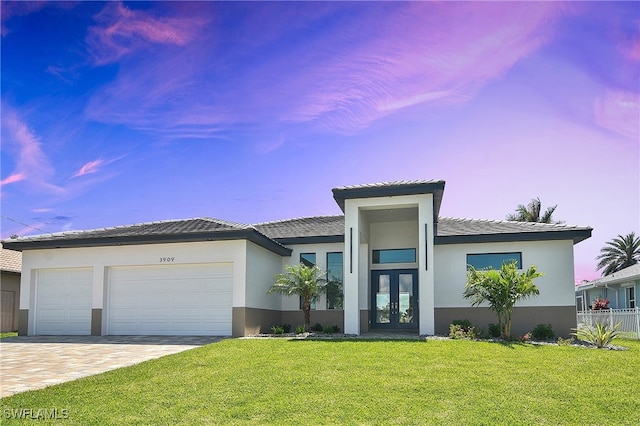 view of front facade featuring french doors, stucco siding, an attached garage, a front yard, and decorative driveway