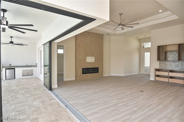unfurnished living room with a ceiling fan, a raised ceiling, ornamental molding, baseboards, and a fireplace