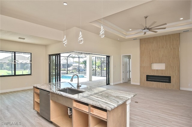 kitchen with a sink, open floor plan, a raised ceiling, light wood-style flooring, and baseboards