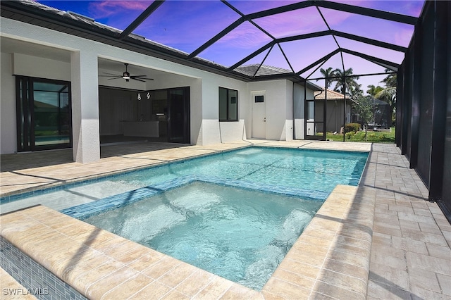 pool at dusk featuring ceiling fan, a patio, a pool with connected hot tub, and a lanai
