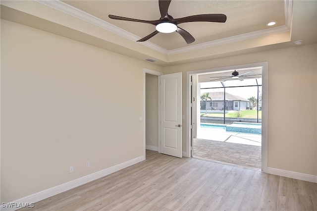 spare room featuring light wood-type flooring, ceiling fan, crown molding, baseboards, and a tray ceiling