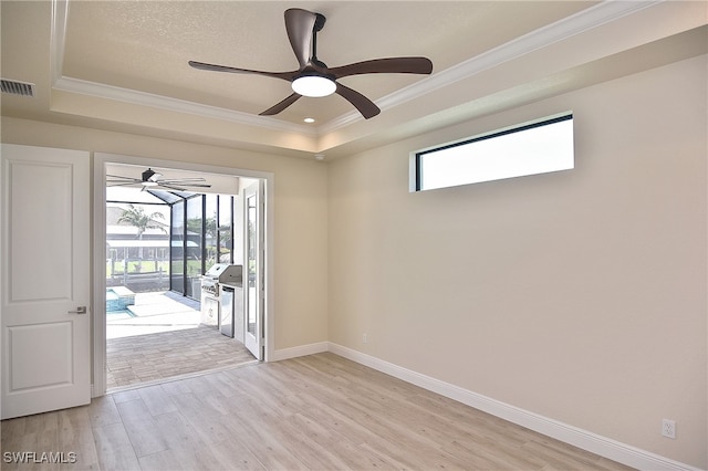 spare room with a raised ceiling, a ceiling fan, light wood-type flooring, ornamental molding, and baseboards