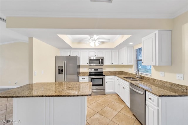 kitchen featuring stainless steel appliances, a sink, a raised ceiling, white cabinets, and dark stone counters