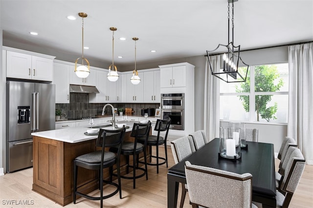 9102 Wisteria Way, Naples, FL 34114 - kitchen featuring appliances with stainless steel finishes, a chandelier, under cabinet range hood, a sink, and decorative backsplash