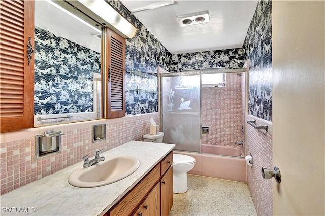 full bathroom with toilet, vanity, bath / shower combo with glass door, tile walls, and speckled floor