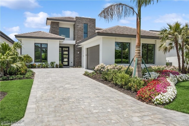 view of front of home with a garage, stucco siding, decorative driveway, a tile roof, and stone siding