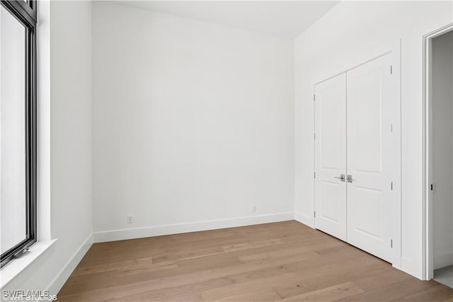 unfurnished bedroom with light wood-style flooring, baseboards, and a closet