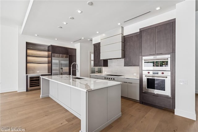 kitchen with appliances with stainless steel finishes, a sink, beverage cooler, tasteful backsplash, and light wood finished floors