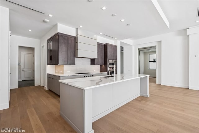 kitchen featuring light wood-style flooring, modern cabinets, black electric stovetop, dark brown cabinetry, and baseboards